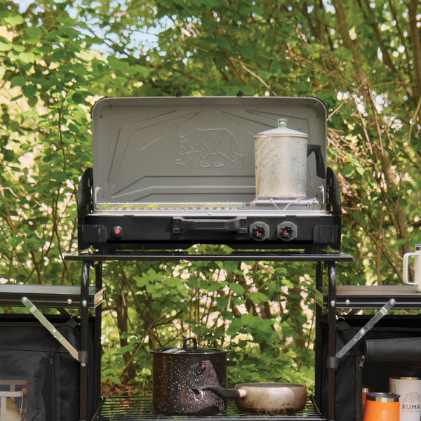 Portable camping stove with pots and pans on a stand in a forest setting