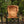An orange padded camping chair with a black metal frame, set in a wooded outdoor environment.