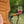 An outdoor camping chair in warm tan with a wine glass resting on its armrest, filled with pink wine, set against a blurred green garden background.