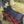 A woman outdoors in a grassy field is demonstrating a black padded camping mat laid over a red and black buffalo plaid collapsible wheeled storage cart.