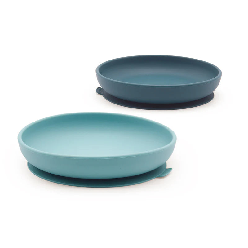 Two round silicone suction plates from the Ekobo Silicone Suction Plate Set for Kids, in blue and teal colors, each featuring a raised edge and a side tab, made from food-grade silicone, displayed on a white background.