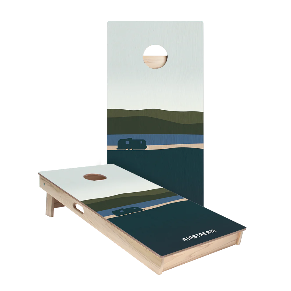 Introducing the Airstream ACA 2 x 4 Star Cornhole Boards—a set of two regulation-sized boards featuring a scenic landscape with hills, a lake, and a charming small trailer. Each board has a classic round hole and is framed in light wood, with “AIRSTREAM” displayed on the lower section of one board. Crafted to meet American Cornhole Association standards for quality and play, these boards are perfect for Airstream enthusiasts.