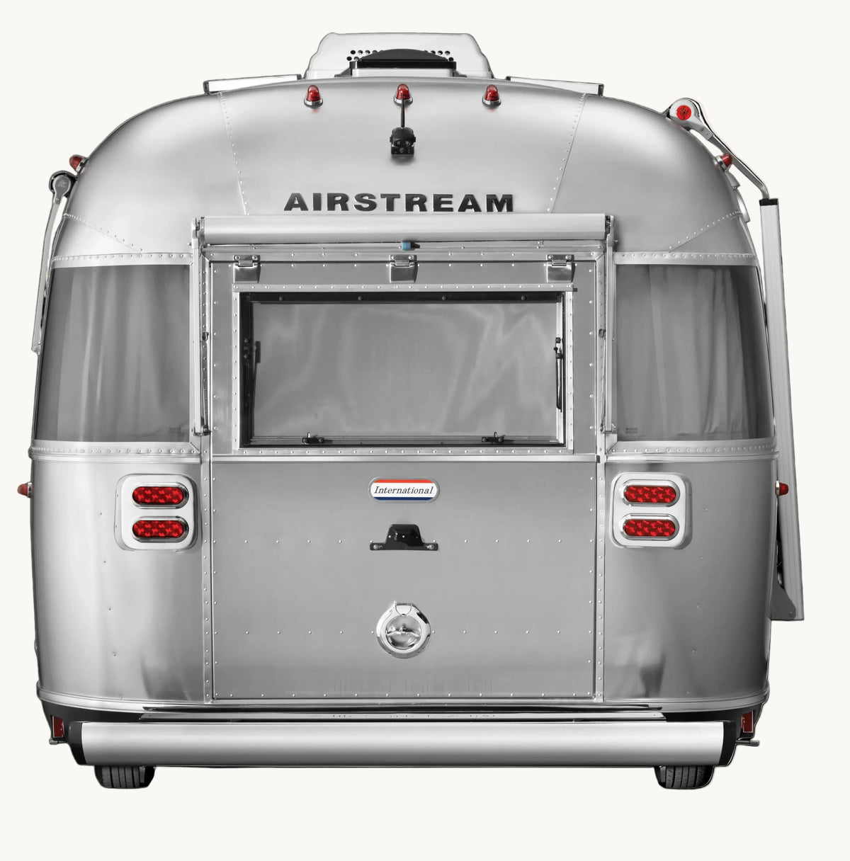 Rear view of a silver Airstream travel trailer on a plain white background, showing the rear window, service window, red taillights, and Airstream branding.