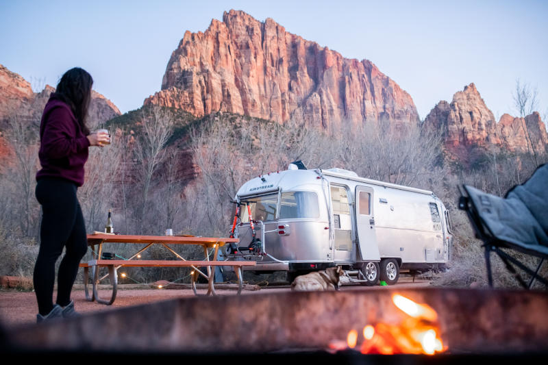 Woman outside looking at an Airstream with mountains in the distance