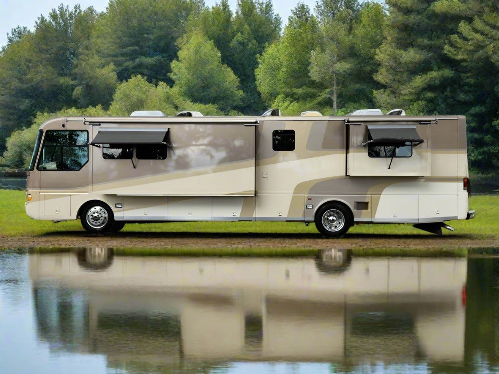 A tan and beige RV is parked beside a pond with a forest in the background. Its reflection shimmers in the still water, and several windows and awnings are open, suggesting a comfortable interior that could be enhanced by features such as Airstream Custom Encasements for A-Series Motorhomes, offering bed bug protection for added peace of mind.