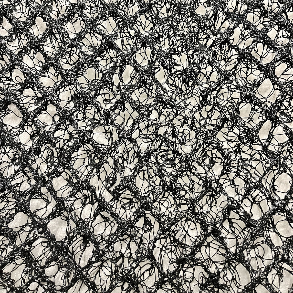 Close-up of a black, tangled net or mesh with irregular, intersecting threads, creating a chaotic, web-like pattern against a light background—reminiscent of the structured design featured in the Airstream Mattress Airflow for Bambi Travel Trailers moisture barrier.