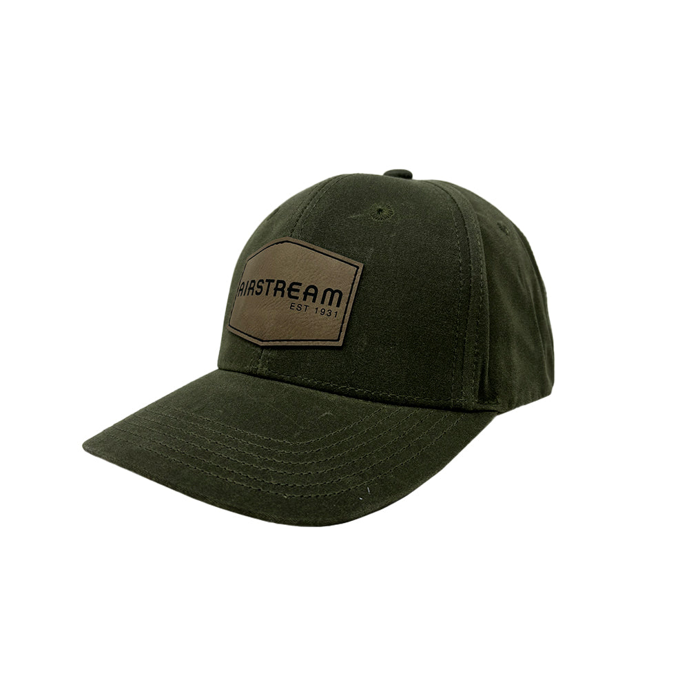 The Airstream 1931 Leather Patch Wax Cotton Hat is a dark green waxed cotton dad cap featuring vintage-style visible stitching, a curved brim, and a brown leather patch on the front that reads “AIRSTREAM EST. 1931.”.