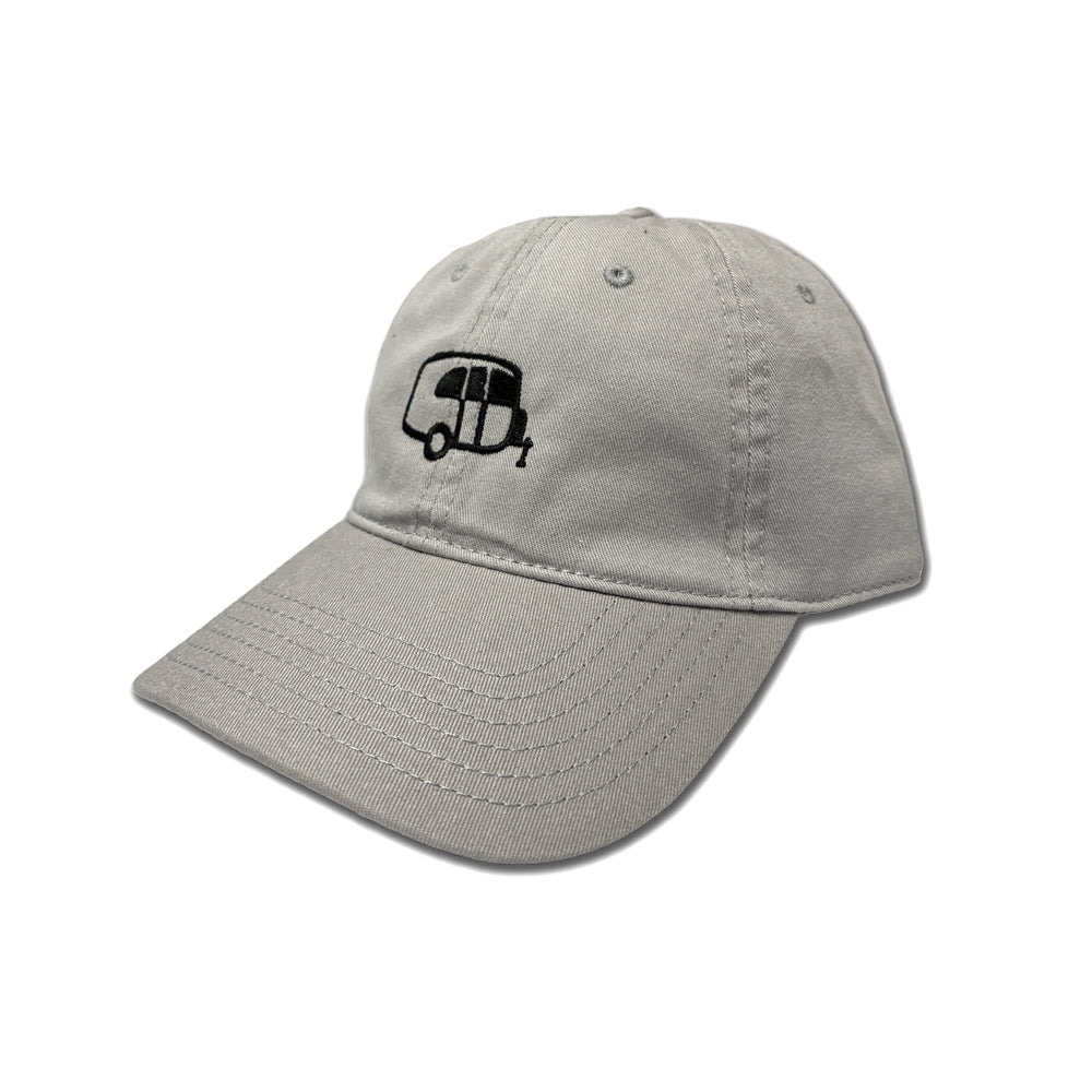 The Airstream Basecamp Outline Hat is a light gray outdoor adventure hat featuring a black embroidered outline of a small trailer, reminiscent of an Airstream Basecamp, on the front. Designed with visible stitching and eyelets on top, the hat is displayed against a white background.