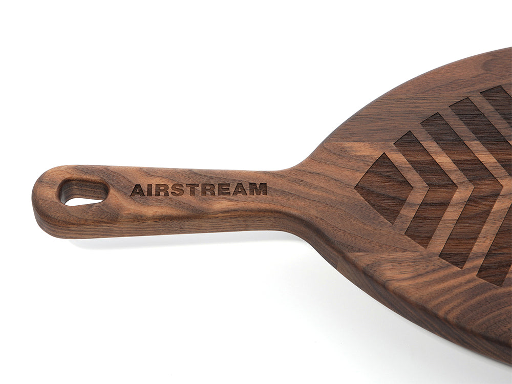 A close-up of the Frank Lloyd Wright x Airstream Charcuterie Board, featuring a geometric pattern inspired by Frank Lloyd Wright carved into the walnut surface and “AIRSTREAM” engraved on the handle.