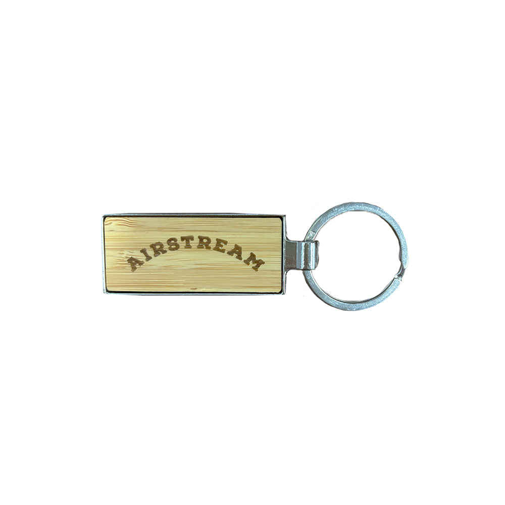 The Airstream Heritage Arc Bamboo Style Keychain features a rectangular bamboo design with “AIRSTREAM” elegantly engraved in an arc and is attached to a metal keyring, displayed against a white background—a unique accessory celebrating classic style.