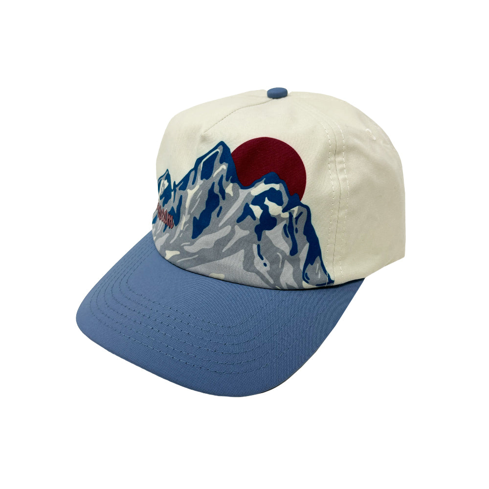 The Airstream Mountain Peak Trucker Hat is a cream and blue adventure hat with a striking front-panel graphic of snow-capped mountains set against a large red sun—perfect outdoor headwear for mountain lovers.