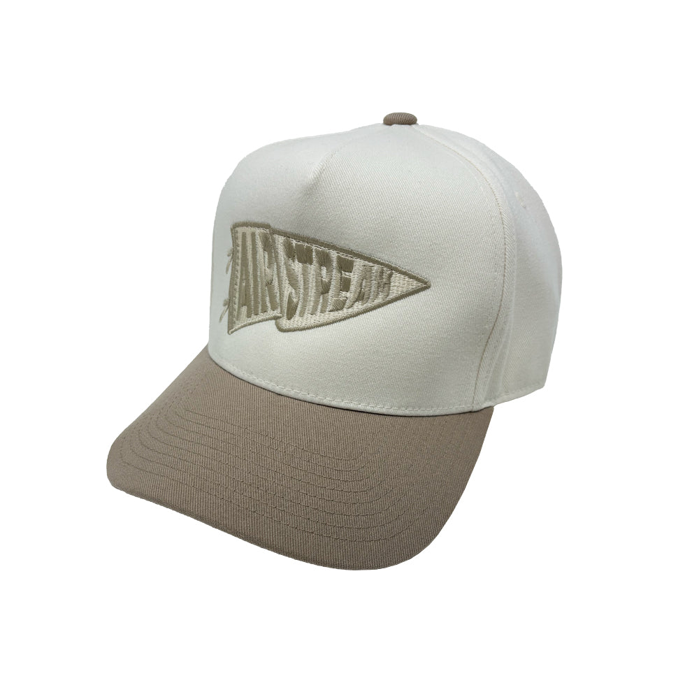 The Airstream Rally Pennant Trucker Hat features a beige and white design with a beige brim and a pennant-shaped embroidered AIRSTREAM logo on the front, blending classic style and comfortable versatility.
