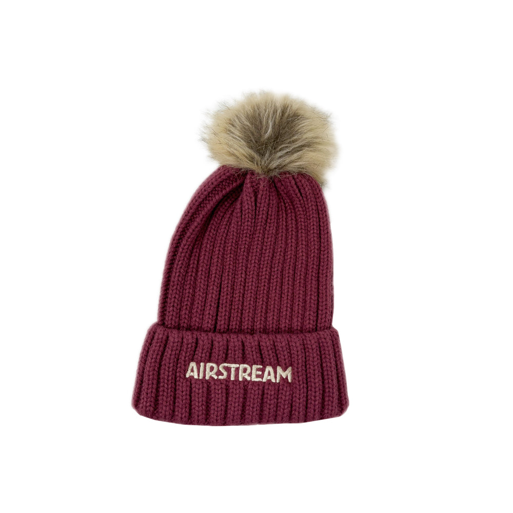 The Airstream Ribbed Pom Beanie in maroon features a folded brim, white AIRSTREAM embroidery, and a brown faux fur pom-pom on top, displayed against a white background.