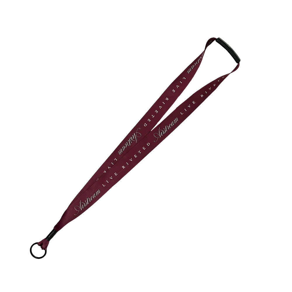 A maroon Airstream Signature Series Lanyard with a metal key ring and black plastic clip, featuring white cursive text that reads Astraea LIVE UNITED repeatedly along the fabric.