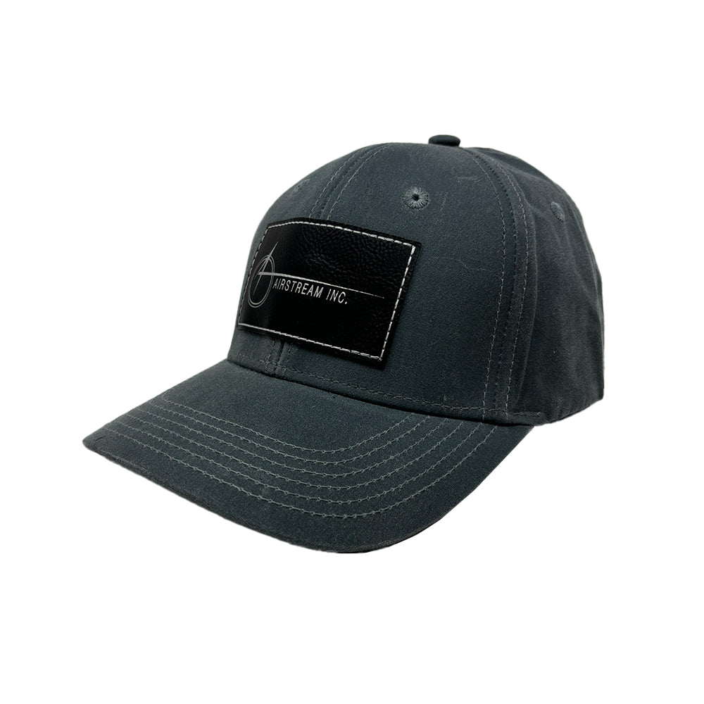 Airstream Space A Leather Patch Wax Cotton Hat crafted from waxed cotton for a subtly distressed, vintage-inspired finish, featuring white stitching and a black rectangular leather patch on the front with a white Airstream logo and “AIRSTREAM INC.” text.