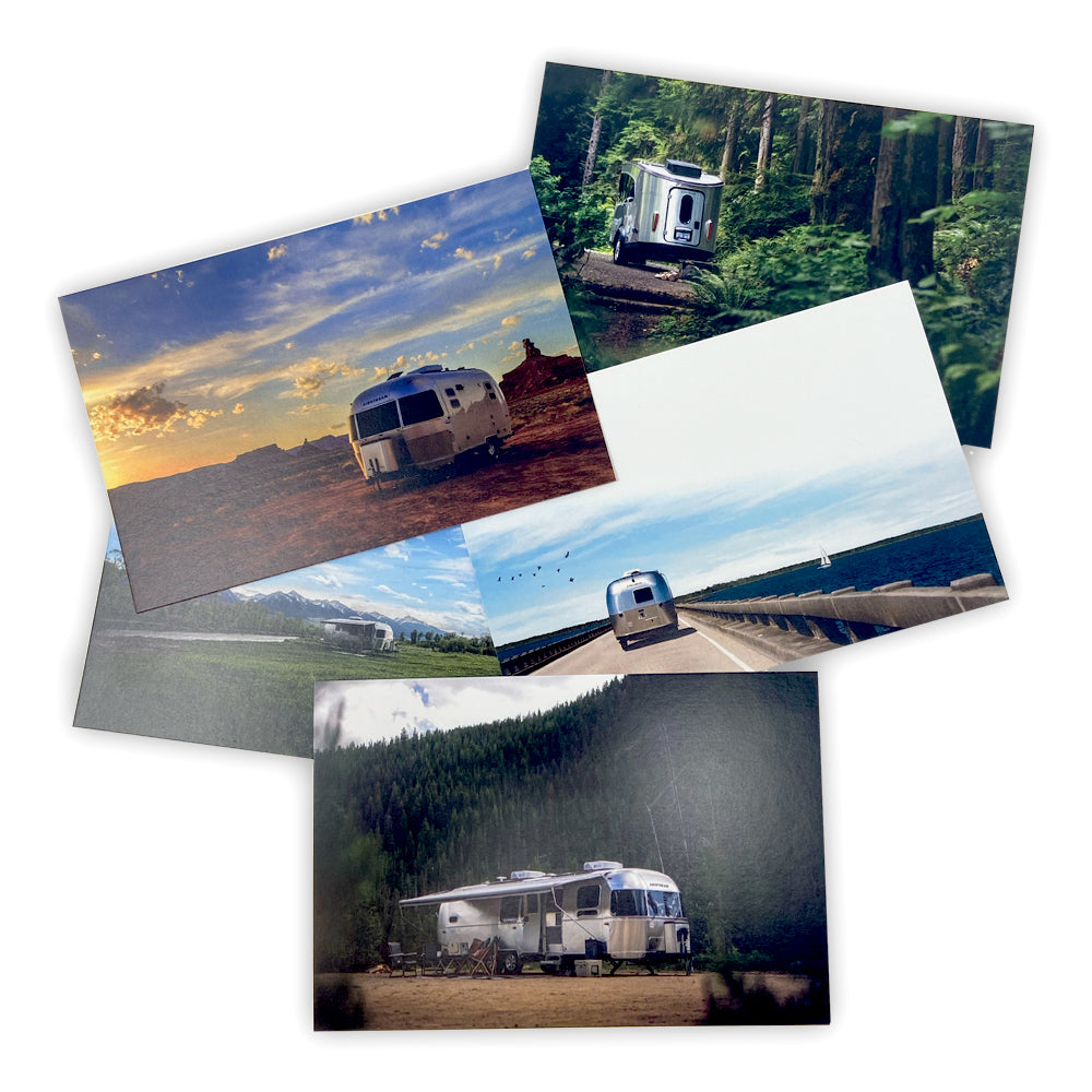 A set of five Airstream Travel Trailer Picturesque Postcards displays silver Airstream trailers in a variety of scenic locations—forests, mountains, a desert, and open roads—scattered across a white background.