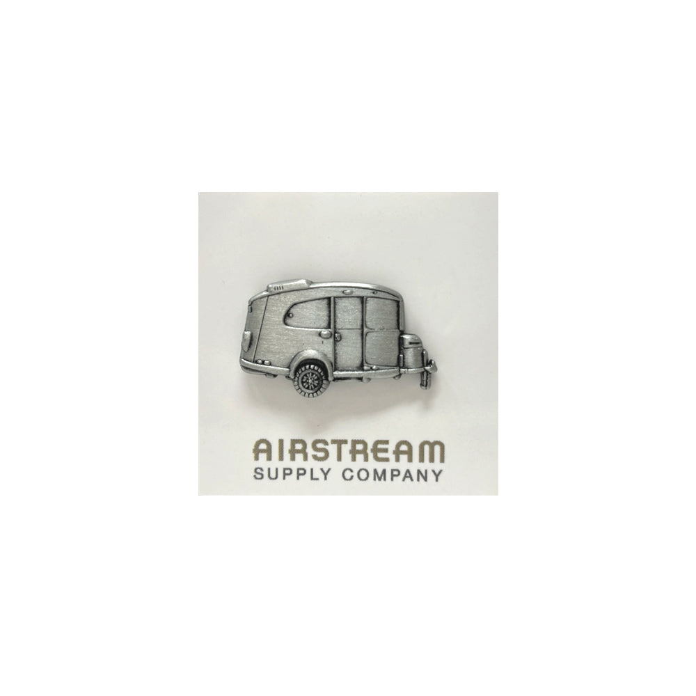 The Airstream Basecamp Pin is a silver adventure pin shaped like an Airstream trailer—reminiscent of the iconic Basecamp model—that rests above the text “AIRSTREAM SUPPLY COMPANY” on a light background, making it the perfect road trip accessory.