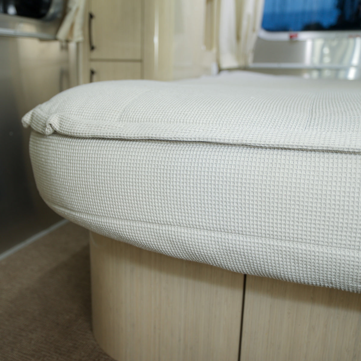 Close-up of a textured, light-colored cushion on a wooden base inside a modern, well-lit RV or camper interior, complemented by Airstream Custom Fit Beddy’s for Quiksilver Travel Trailers for added comfort and style.
