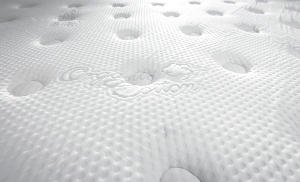 Close-up view of a white, textured mattress surface with circular indentations and embossed text reading Organic Cotton..
