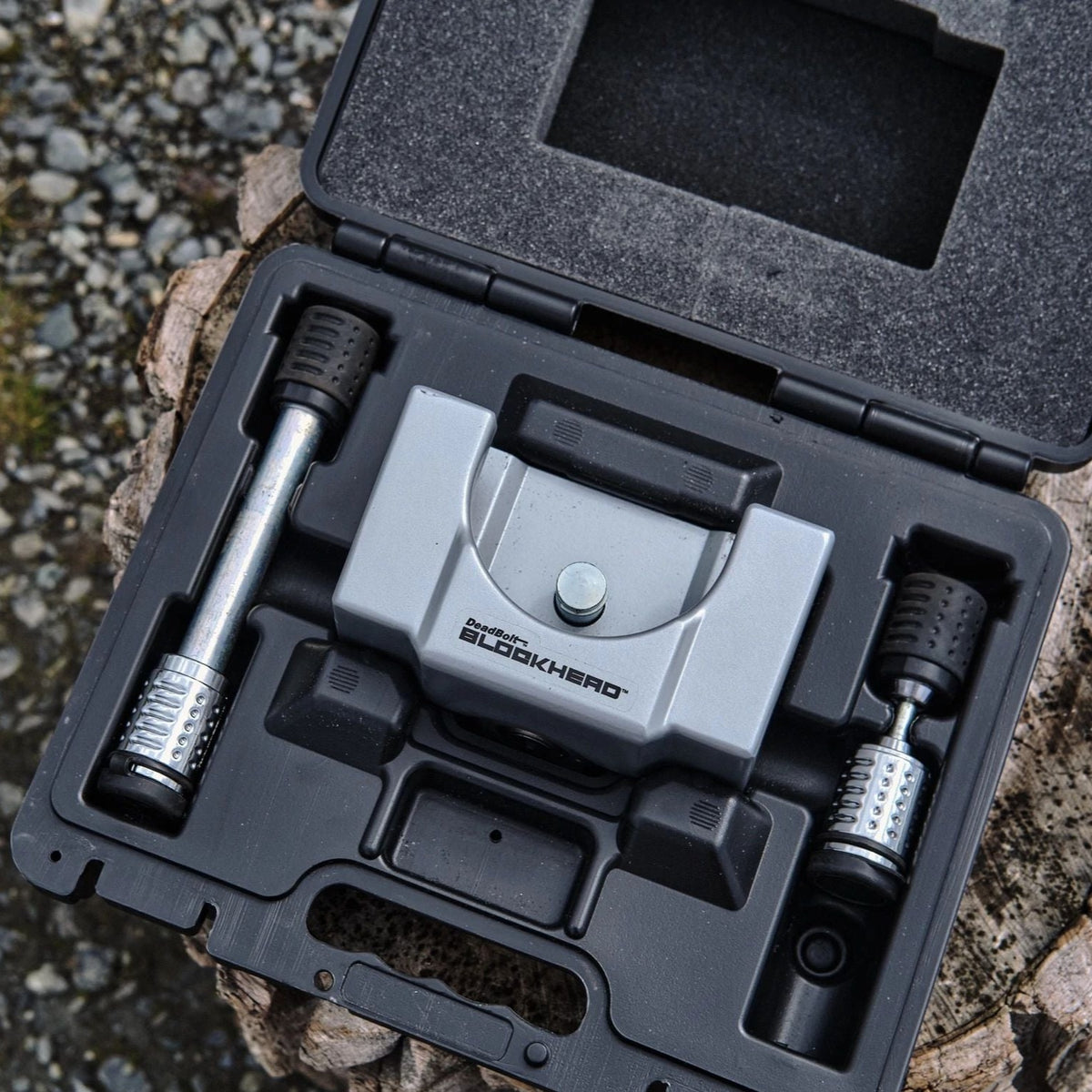 Open black carrying case containing the Airstream Anti-Theft Hitch and Trailer Lock Kit, featuring a sturdy metal Blockhead device and two metal handles with textured grips—each securely arranged in custom foam cutouts on a rugged outdoor surface—an essential lock kit for enhanced Airstream travel trailer security.