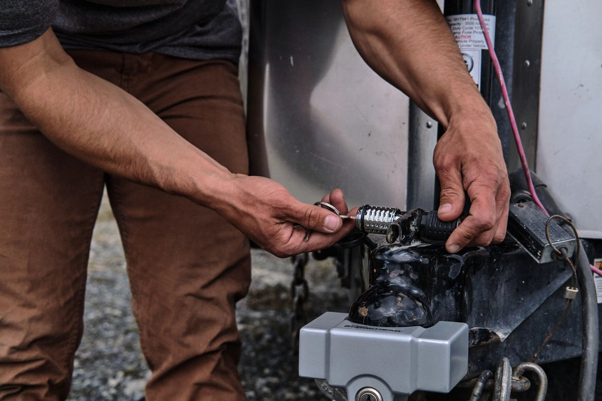 A person uses a key to unlock the Airstream Anti-Theft Hitch and Trailer Lock Kit on a travel trailer. Their hands are focused on the lock mechanism, while some wiring is visible in the background, highlighting attention to Airstream security.