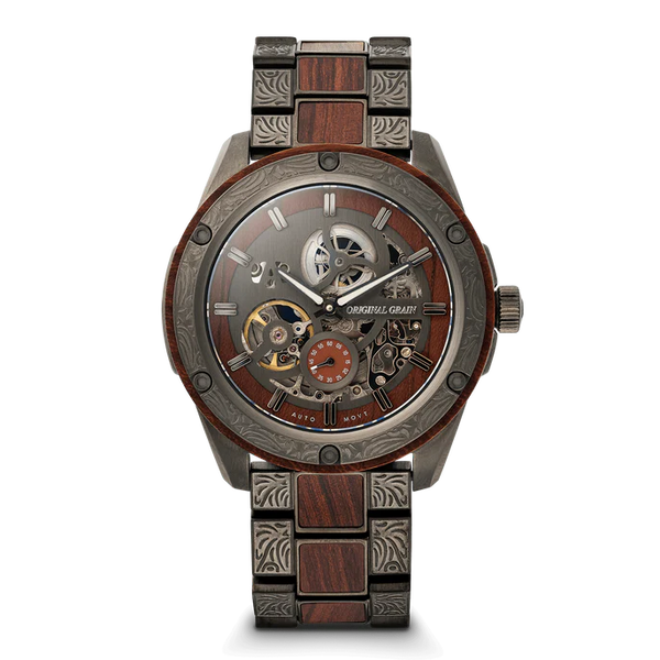 A luxury skeleton wristwatch with a dark wood and gunmetal steel link bracelet, featuring a detailed open-heart dial with visible gears and a small orange sub-dial. The brand name 'OAKRIVL GRAND' is printed on the dial.