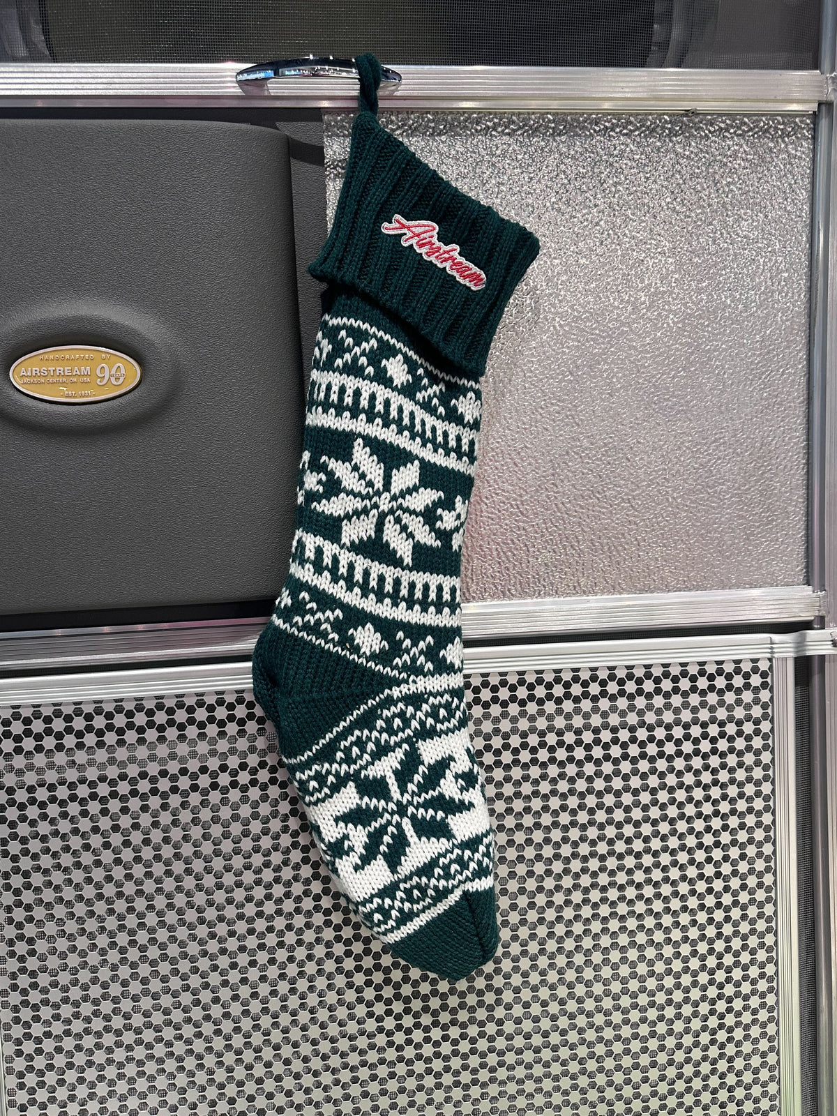 Airstream Holiday Stocking: Add festive cheer to your holiday décor with this green and white knit Christmas stocking, adorned with snowflake patterns and a red Alabama patch near the top. Its unique blend of colors and details makes it a spirited accent for any space, especially when displayed on a metallic wall.