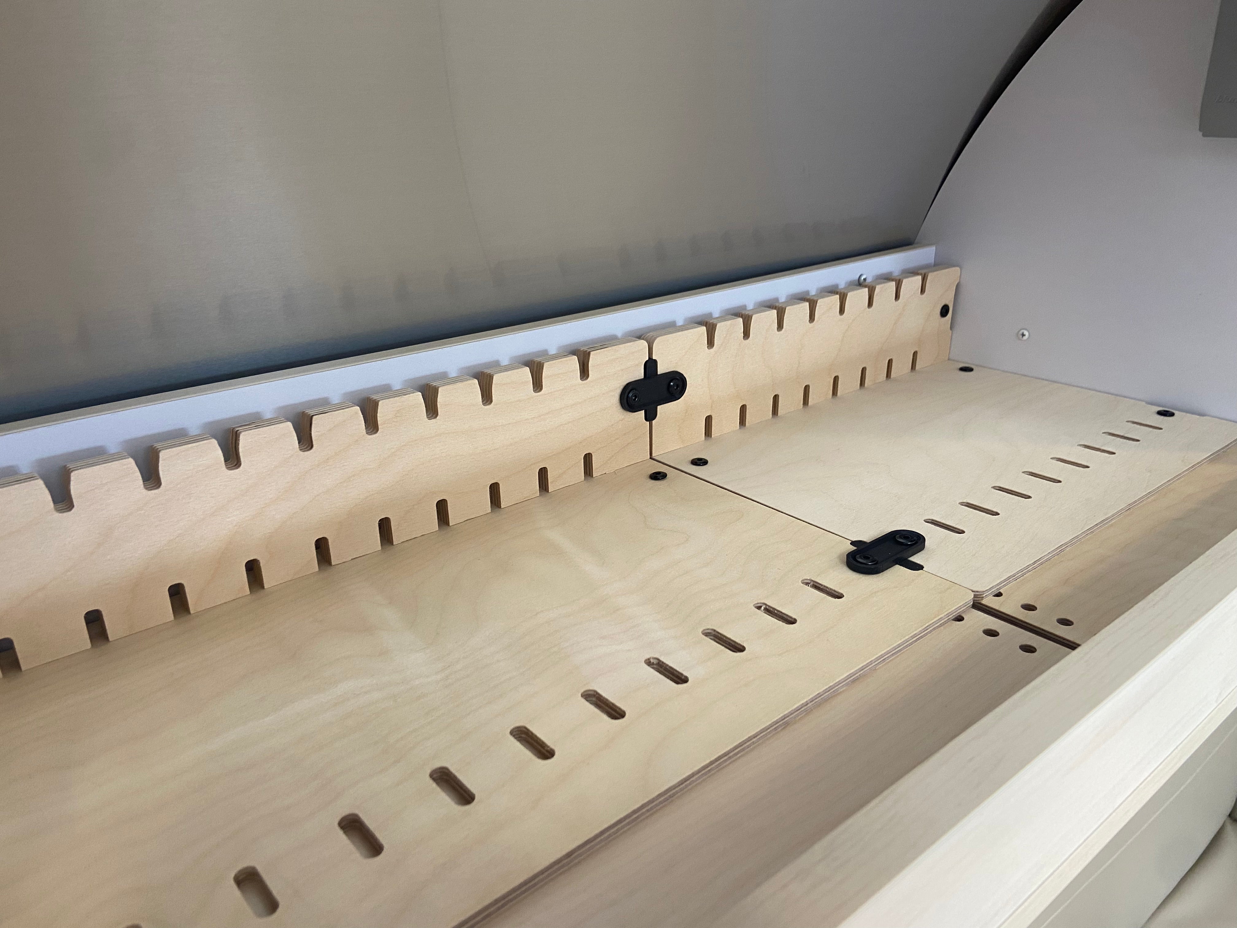 Close-up of a wooden interior section with interlocking notches, hinges, and adjustable slots—distinctive features of the Airstream Touring Coach Roof Locker Organization by Airworthy Equipment Company—set against a curved metallic or plastic background.