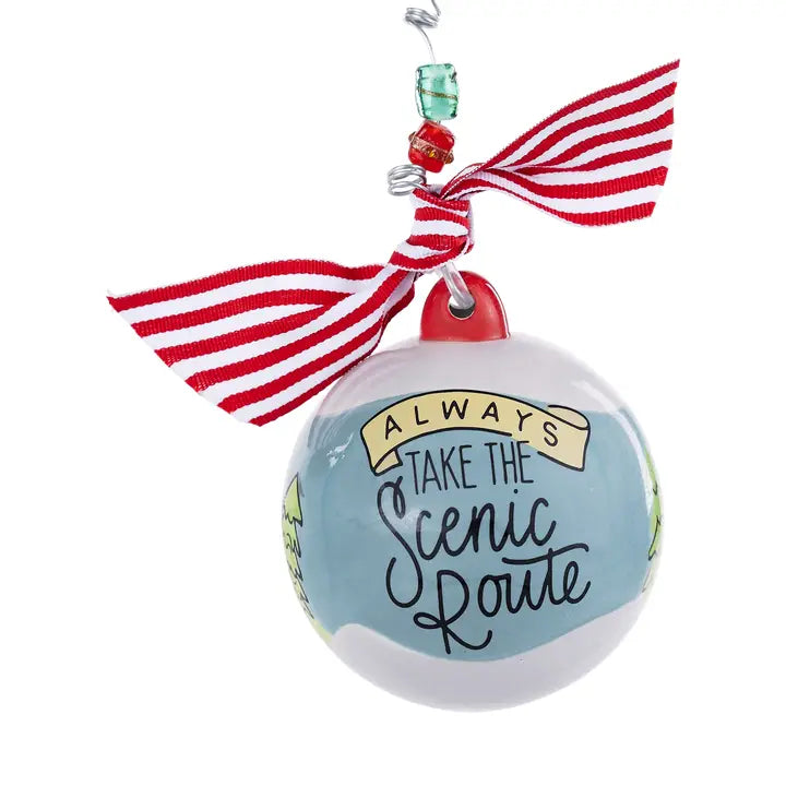The Always Take the Scenic Route Christmas Ornament is a round ornament adorned with a red and white striped ribbon and beads, featuring the phrase “Always take the scenic route” on a blue background—making it an ideal travel keepsake for adventure lovers.