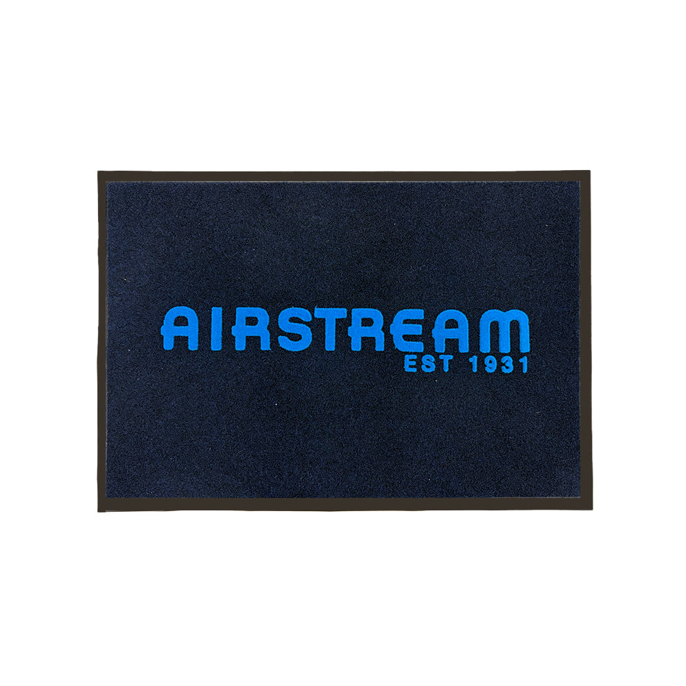 The Airstream Decorative Outdoor Entrance Mat is a rectangular, dark-colored mat featuring a black border and the words “AIRSTREAM” and “EST 1931” in bold blue letters at its center. This durable outdoor entry mat is an ideal way to add style to your travel trailer setup while welcoming guests in classic Airstream fashion.