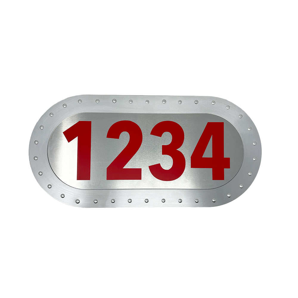An Airstream BRN Plate features an oval metallic design with a silver background, bordered by rivets and prominently displaying the number 1234 in large, custom Big Red Numbers—evoking the iconic style of classic aluminum license plates.