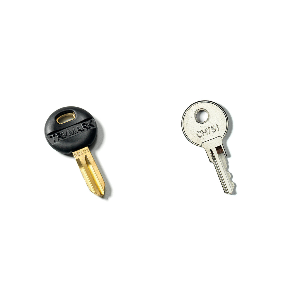 Two keys from the Airstream Cut Key Bundle for Basecamp Travel Trailers are shown on a white background: the left key features a black plastic head labeled “TAYMARK,” while the right key is all metal with “C1751” engraved on its circular head. These keys can serve as spare or pre-cut options for your Airstream Basecamp.