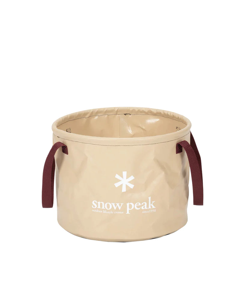 The Snow Peak Camping Jumbo Bucket is a beige, round, collapsible camp bucket with maroon handles on each side and “snow peak” printed in white on the front, perfect for outdoor recycling or storing up to six gallons of gear.