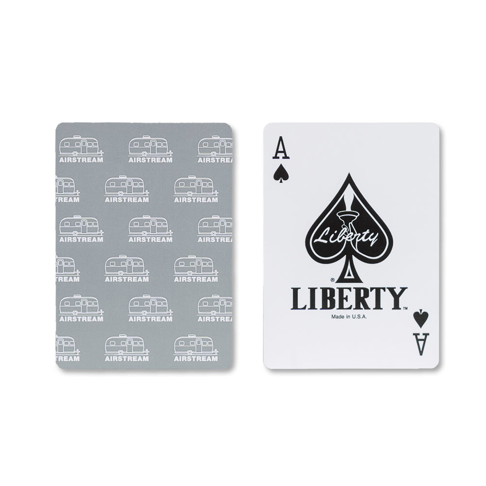 Showcasing two playing cards from the Airstream Card Deck With Case: the back displays a sleek gray pattern decorated with white Airstream trailers, while the front reveals an Ace of Spades marked “Liberty,” featuring a large spade symbol with “Liberty” written within it. This distinctive travel-themed card game comes as part of the stylish Airstream Card Deck With Case, making it perfect for adventures on the road.