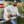 A man with sunglasses and a beard strums an acoustic guitar as he sits on the bumper of a silver Airstream trailer in a grassy outdoor setting, dressed in the Airstream Tonal Comfort Wash Crew Sweatshirt for that perfect touch of vintage style.
