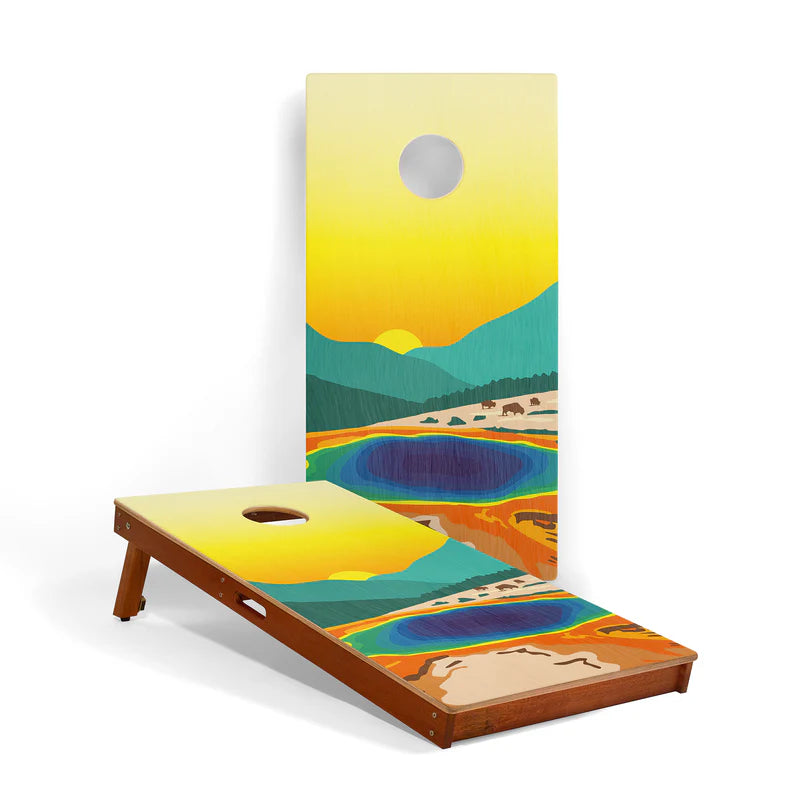The National Parks 2x4 Cornhole Boards by Elakai are perfect for outdoor games, featuring a colorful landscape painting with mountains, a sunset, trees, and a vibrant blue lake. Each portable board has a circular hole near the top, making this cornhole set both visually striking and ideal for gatherings.