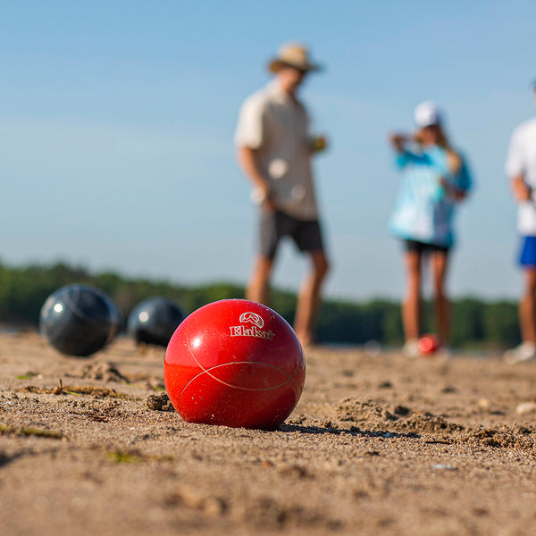 Red Elakai Bocce Ball In The Sand With People Playing In The Background