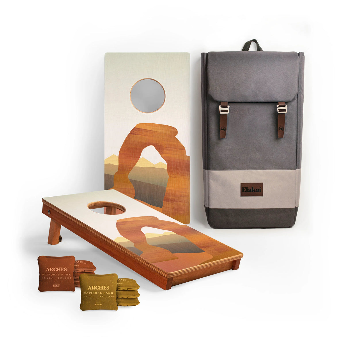 The National Parks Travel Size Cornhole Boards by Elakai include two upright arch-designed boards, eight bean bags, and a gray and brown carrying backpack. Inspired by National Parks, this travel-size set is shown upright and flat against a white background.