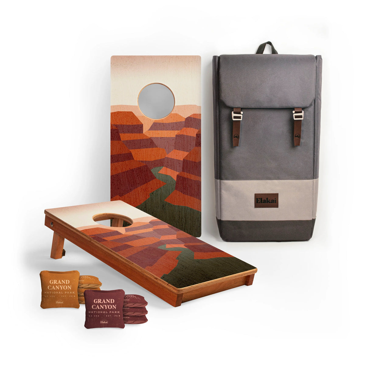 Travel size National Parks Cornhole Boards by Elakai feature painted boards with a canyon landscape, four Grand Canyon-labeled bean bags, and a gray backpack with brown accents—all shown against a white background. Ideal for outdoor adventures, this set brings the beauty of iconic landscapes to your next excursion.