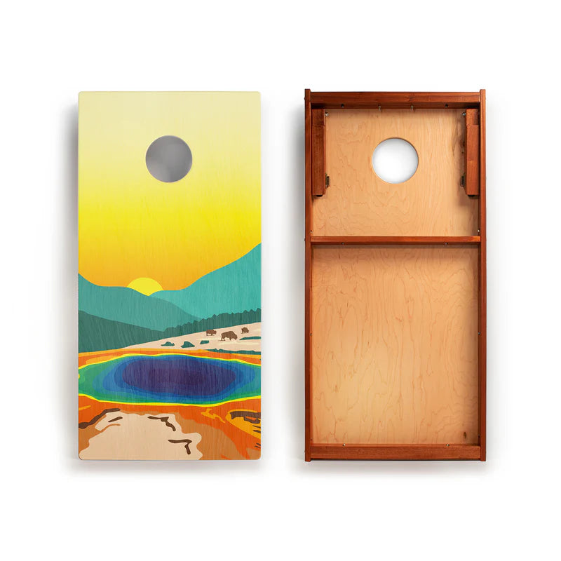National Parks 2x4 Cornhole Boards by Elakai: one board displays a vibrant landscape design with mountains, a pool, and bison, while the other is shown flipped to reveal its plain wood surface and sturdy underside construction. This portable set is ideal for outdoor games, with both boards featuring classic circular holes near the top.