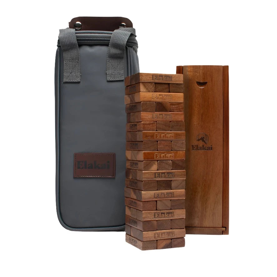 The Acacia Mountain Blocks game, ideal as a Giant Blocks Game for outdoor fun or tabletop gatherings, is shown with a tall carrying bag featuring gray straps and a wooden storage box. The Elakai brand appears on the bag, blocks, and box.