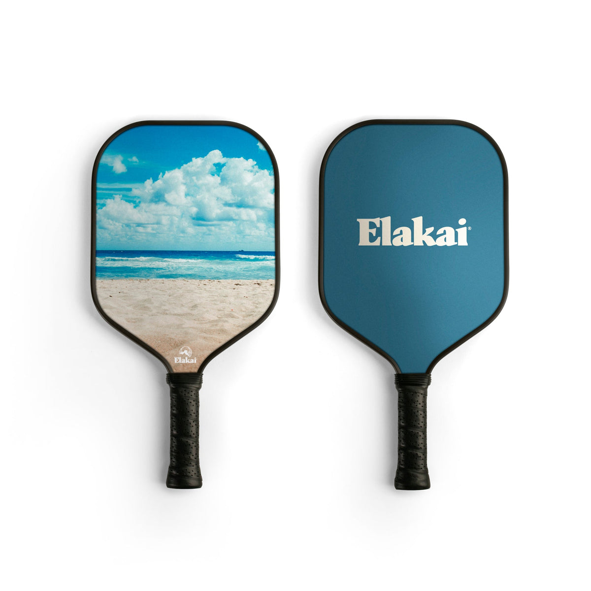 Two pickleball paddles: one, the 13MM Beach Surf Pickleball Paddle, features a beach and sky scene; the other is solid blue with “Elakai” written in white. Crafted from high-performance materials, both Elakai Pickleball Paddles have black handles and are displayed side by side on a white background.