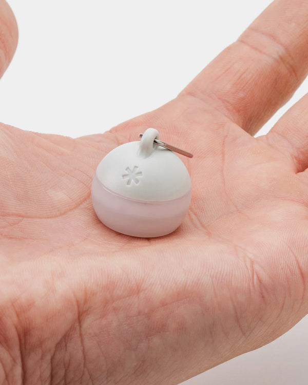 Small white device with a keychain attachment held in a hand against a neutral background