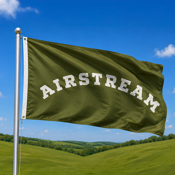 Green flag with 'Airstream' text waving in the wind against a blue sky and green landscape.