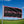 Black flag with pink 'Airstream' logo on a pole against a blue sky and green field.