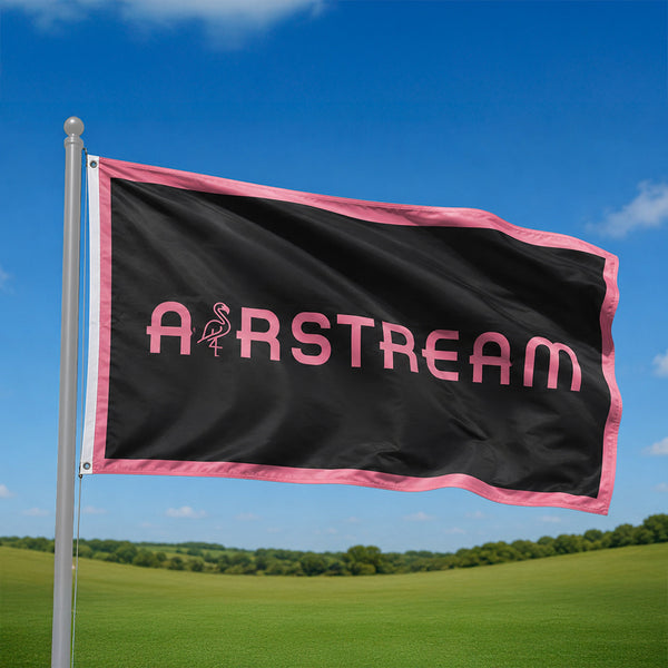 Black flag with pink 'Airstream' logo on a pole against a blue sky and green field.