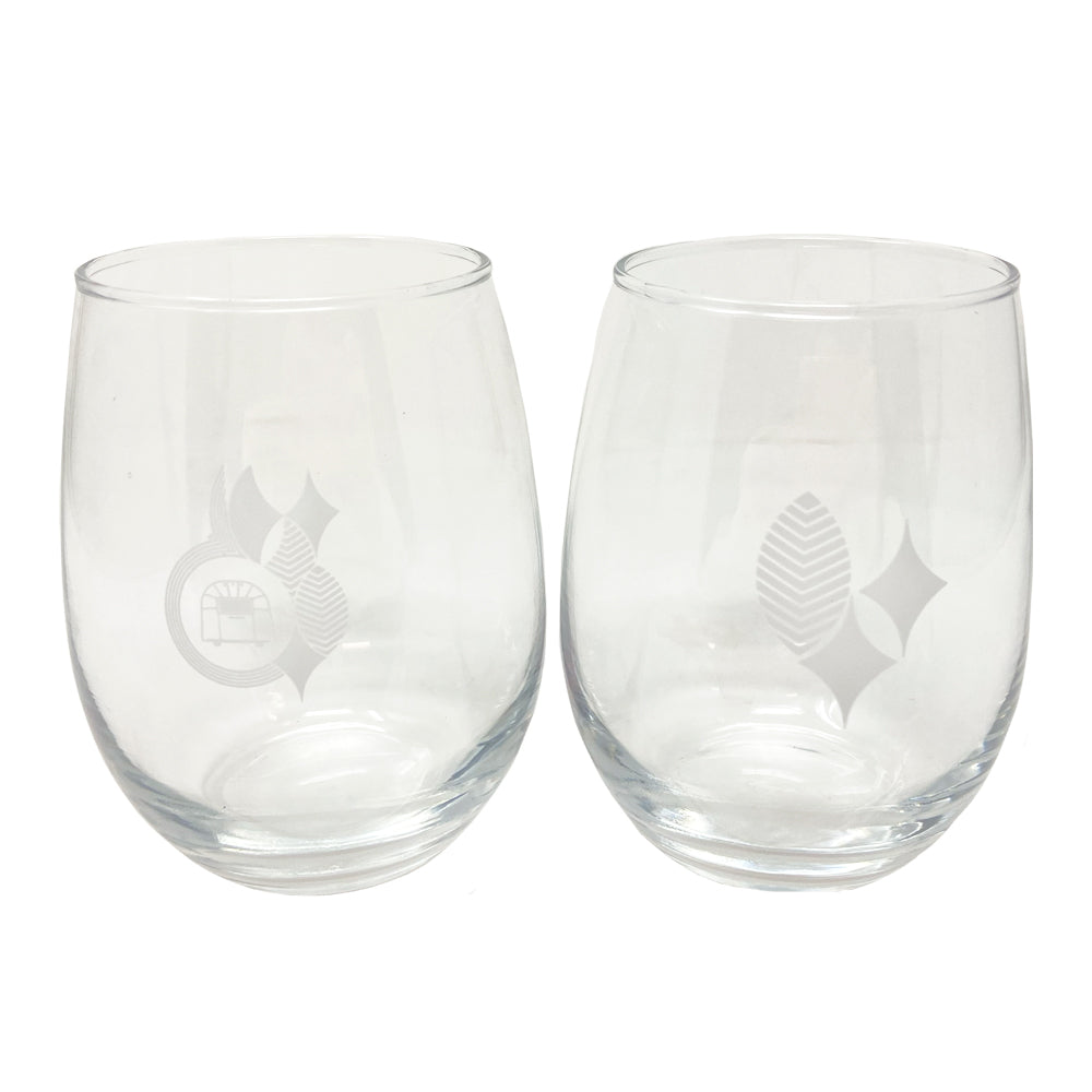 The Frank Lloyd Wright x Airstream Wine Glass Set features two clear stemless wine glasses, each etched with subtle geometric designs inspired by Frank Lloyd Wright’s iconic style—one adorned with overlapping circles and lines, and the other displaying leaf and diamond motifs. Both empty glasses are shown side by side on a white background.