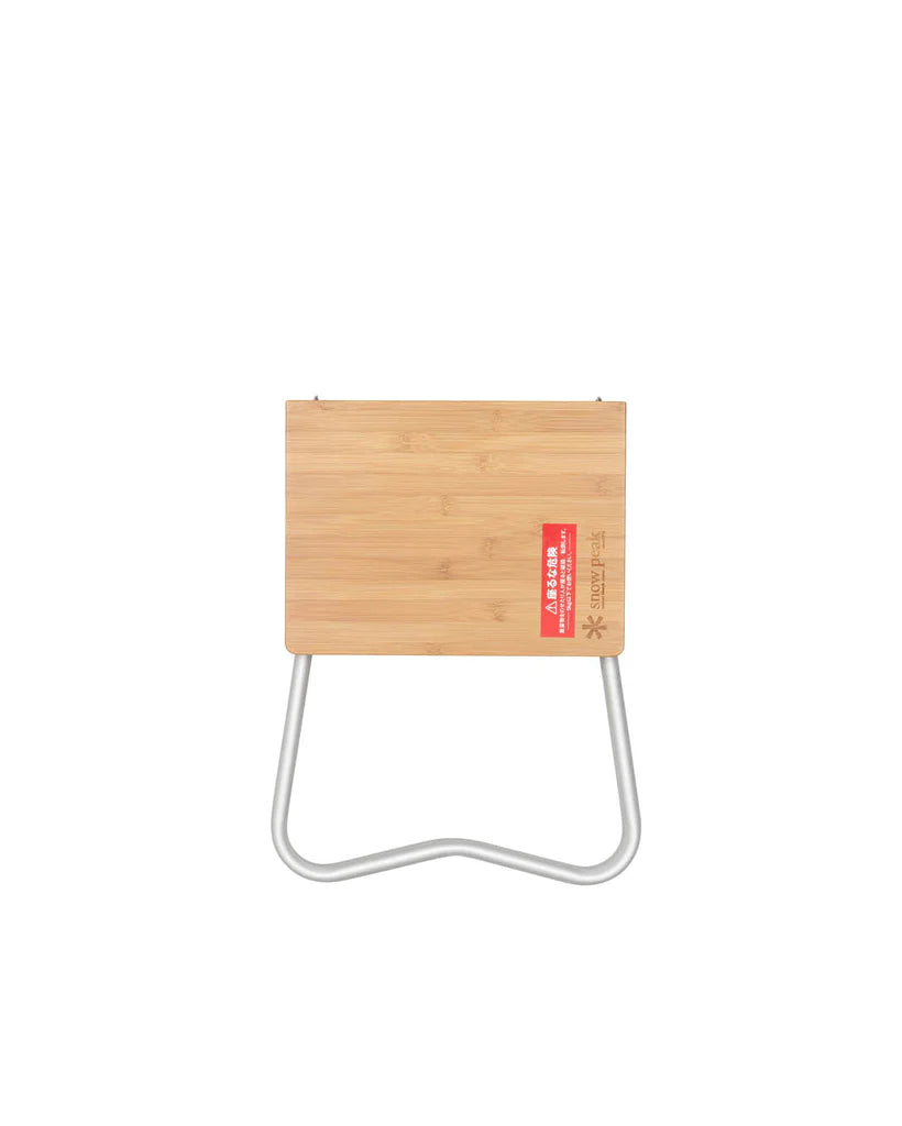 A compact, rectangular Snow Peak Renewed Bamboo My Table with a light bamboo top and curved silver metal legs, viewed from above, featuring a red and white label on one corner.