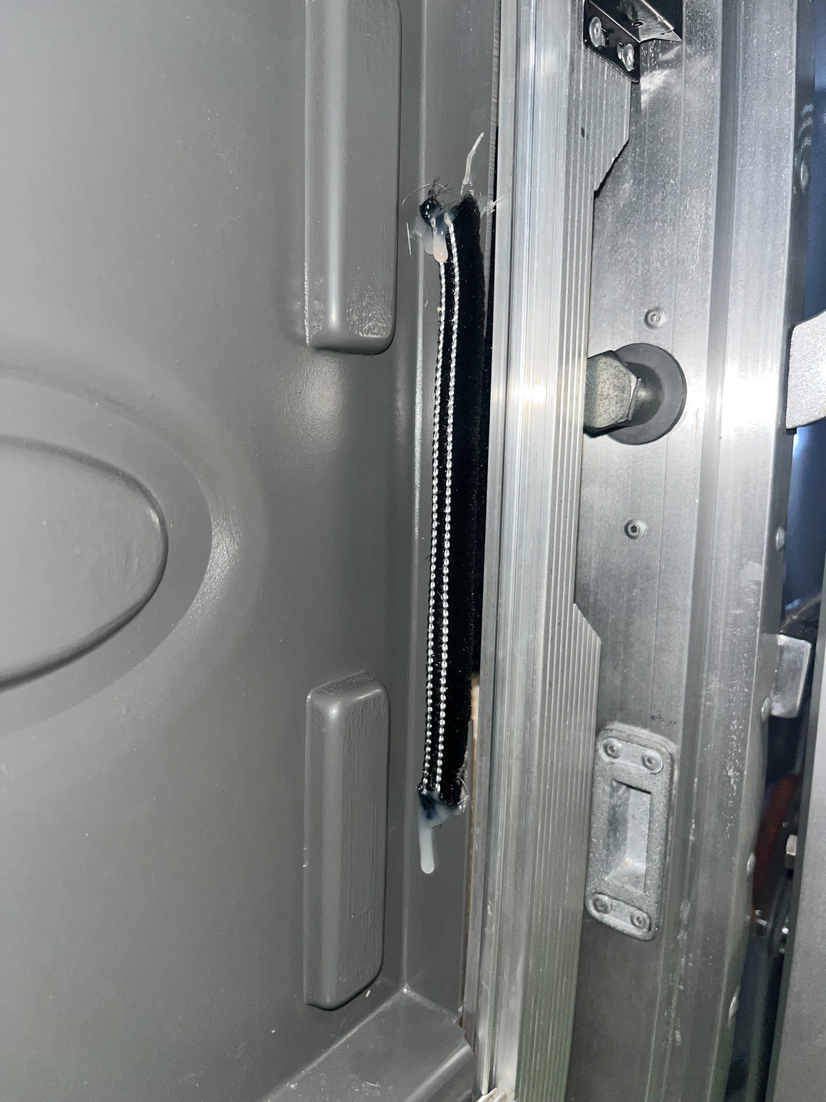 Close-up of a gray metal door edge with a zipper-like black and silver strip (Airstream Fuzzy Window Arm / Bug Seal, Part # 683946-01) that appears partially detached, exposing the inner edge and some damage to the material—possibly indicating the need for a replacement seal.