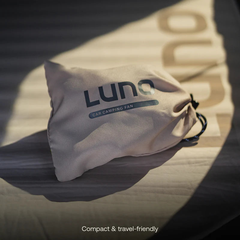 A beige drawstring bag labeled USB Powered Camping Fan by Luno rests on a light surface with shadows, the word “Luno” partly visible. Text reads: Compact & travel-friendly—perfect for van life and car camping, this USB-C powered fan keeps you cool on the go.